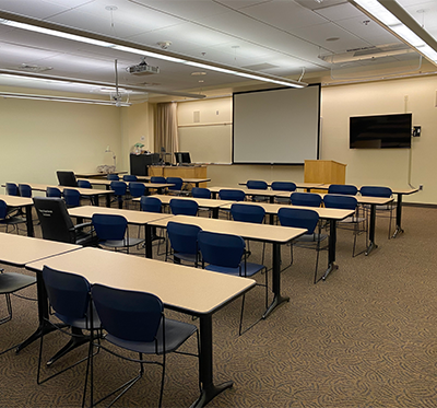 Chairs behind rows of long tables facing a screen and lecturns