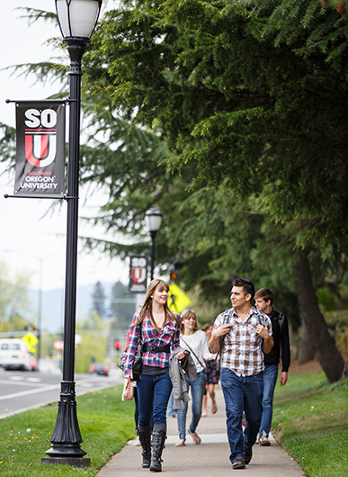 students walking and talking on campus with SOU sign visible on lamp post